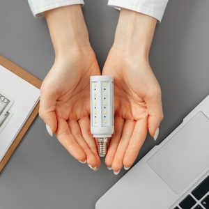 Female hand holding a light bulb above the table Female hand holding a light bulb above the working table